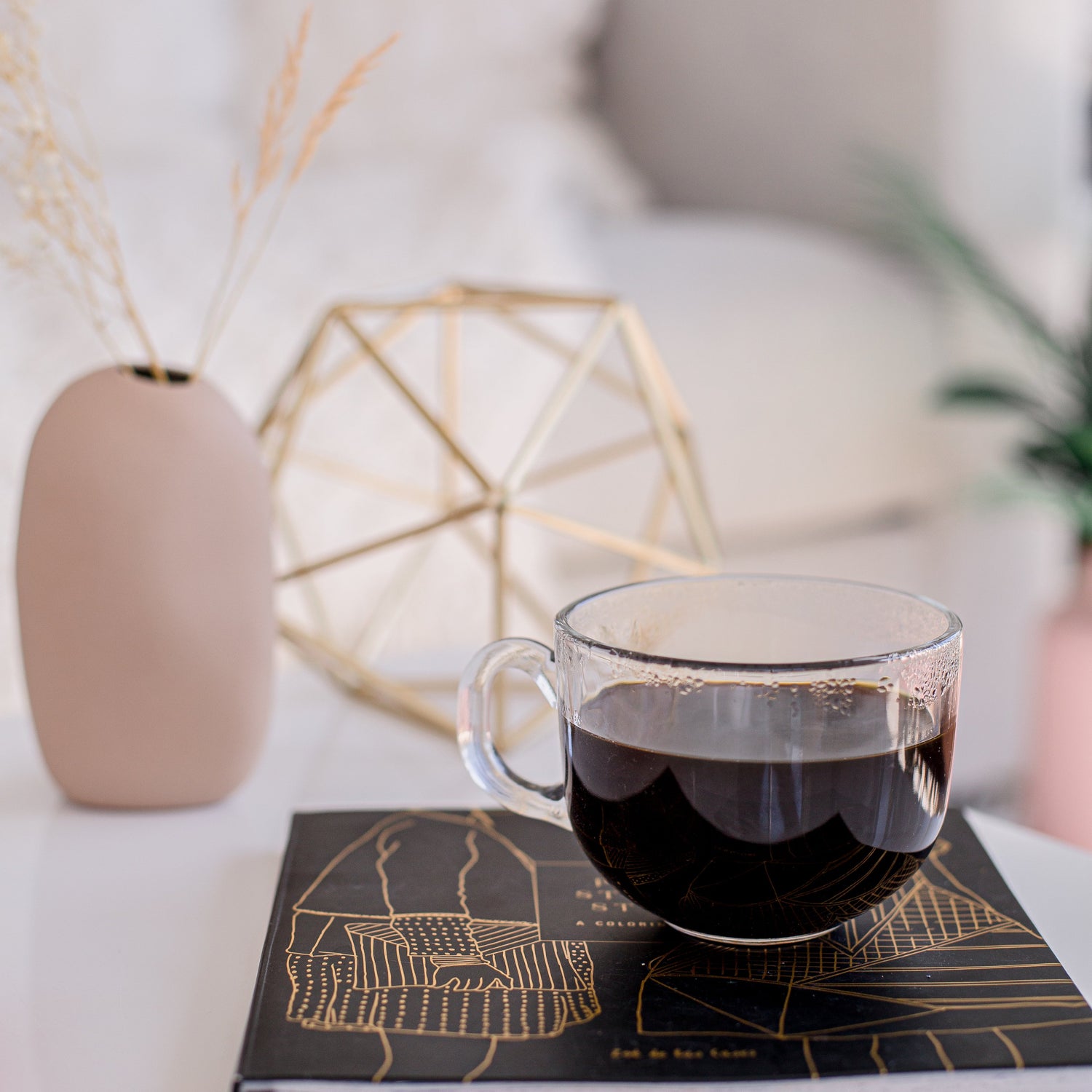 Clear glass mug with dark liquid on a decorative book in a cozy indoor setting